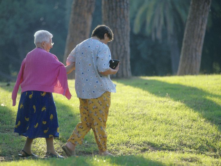 Nella foto si vedono una signora anziana con la sua badante mentre fanno una passeggiata in un parco
