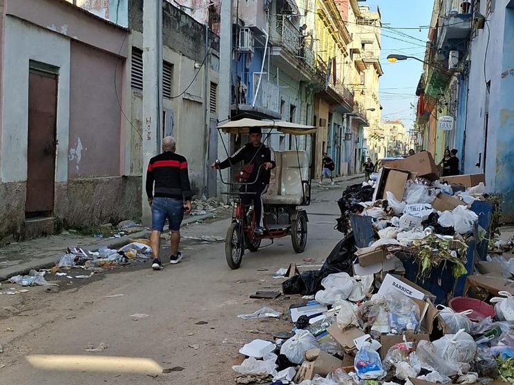 Nel centro dell'Avana semi-deserto un ragazzo guida un bici-taxi mentre un anziano si allontana. Una montagna di rifiuti giace sul ciglio della strada