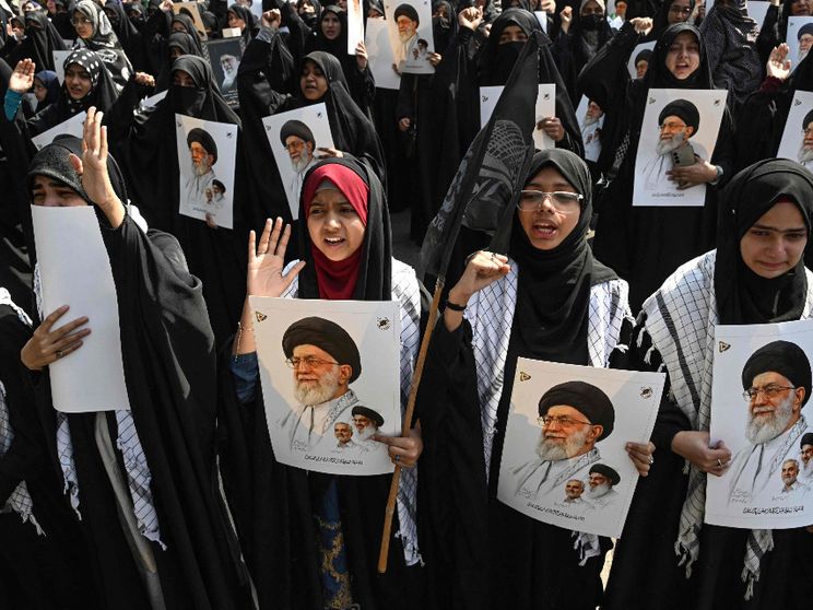 Una folla di donne con il lungo abito nero e la testa velata tengono in mano fotografie di Khamenei in segno di protesta