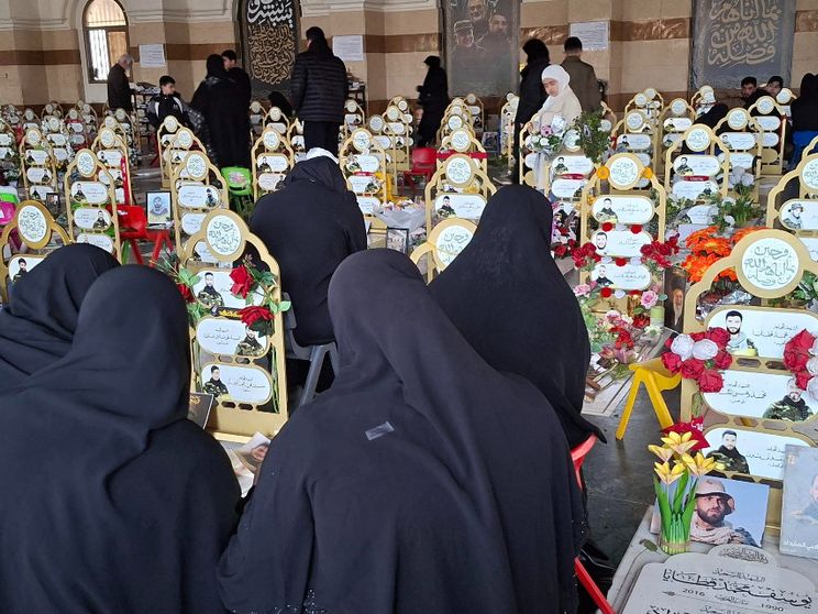 Donne velate di nero, di spalle davanti alle tombe ornate di nastri gialli e fiori con le fotografie di giovanissimi