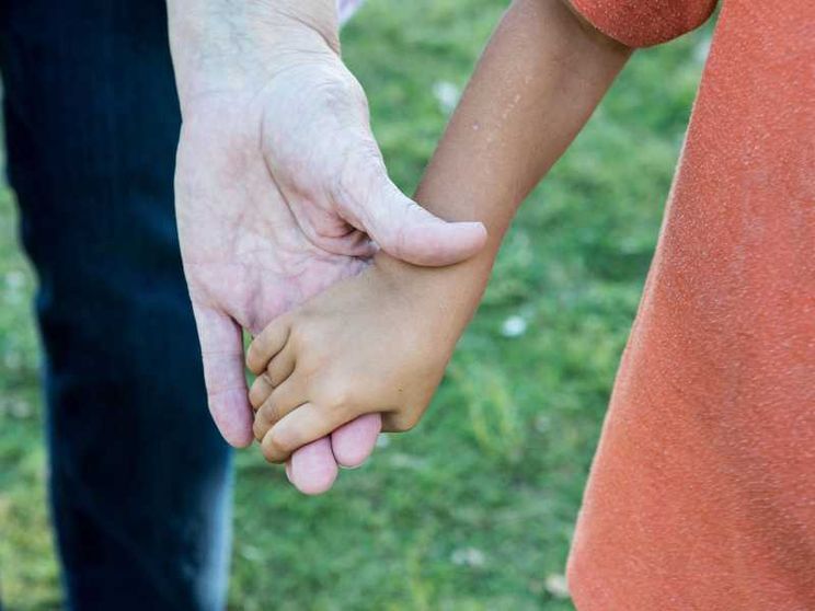 Due mani che si stringono: quella di un adulto e di un bimbo adottato