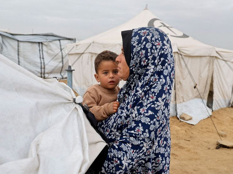 Una donna con in braccia il figlio in una tendopoli per sfollati a Khan Younis, nel sud della Striscia di Gaza