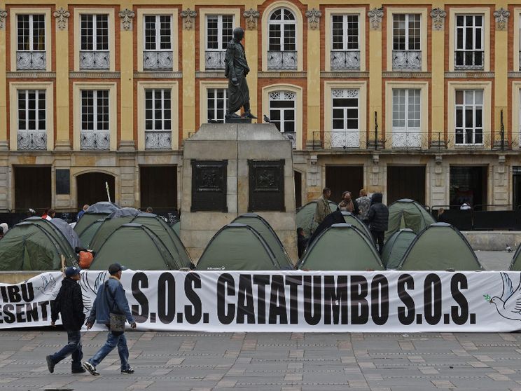 Due persone passano davanti a una serie di tende nella piazza Bolívar di Bogotà e alla scritta: "S.O.S. Catatumbo". Con l'iniziativa, i promotori hanno voluto denunciare la violenza nella regione ocolombiana
