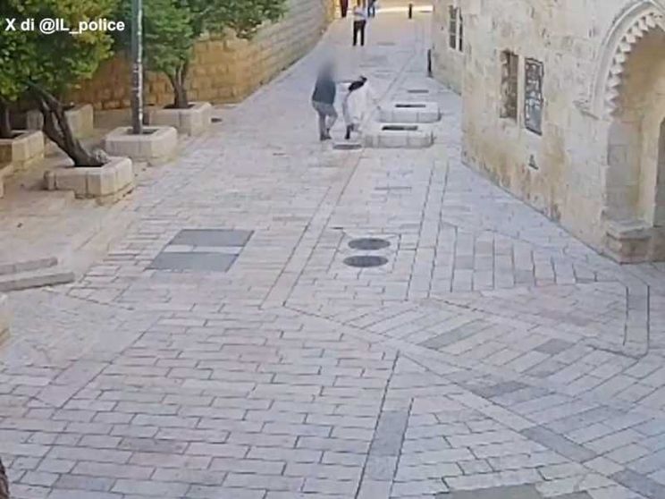 Una vasta via piastrellata, con pochissime persone: un uomo aggredisce alle spalle una suora in abito bianco e velo nero