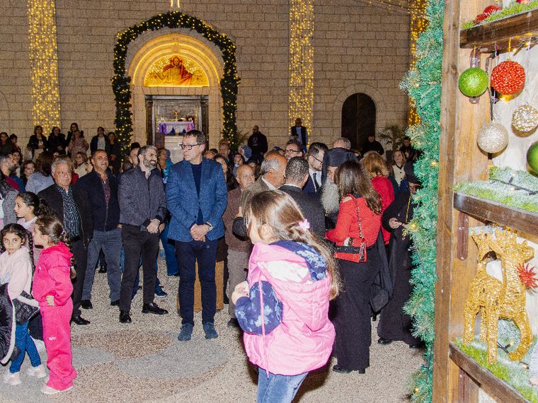 Bambini e adulti chiacchierano e sorridono in una piazzetta davanti alla chiesa addobbata con luci e decorazioni natalizie