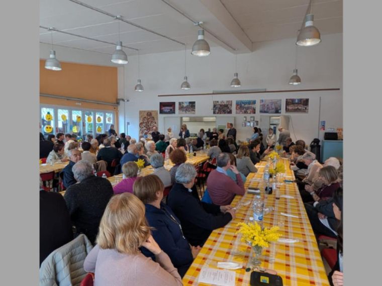 Più di cento persone sono sedute al tavolo; sono lunghe tavolate con tovaglie colorate. Si condivide il pasto.