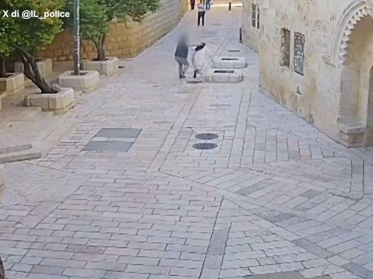 Una vasta via piastrellata, con pochissime persone: un uomo aggredisce alle spalle una suora in abito bianco e velo nero