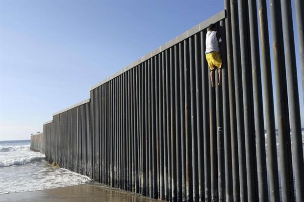 Un giovane migrante dall'Honduras scala il muro di frontiera a Tijuana (Ansa)
