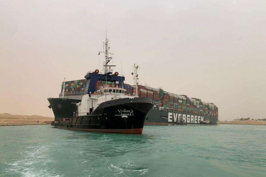 Un'immagine del cargo incagliatosi nel Canale di Suez, sullo sfondo, e in primo piano un'imbarcazione di soccorso