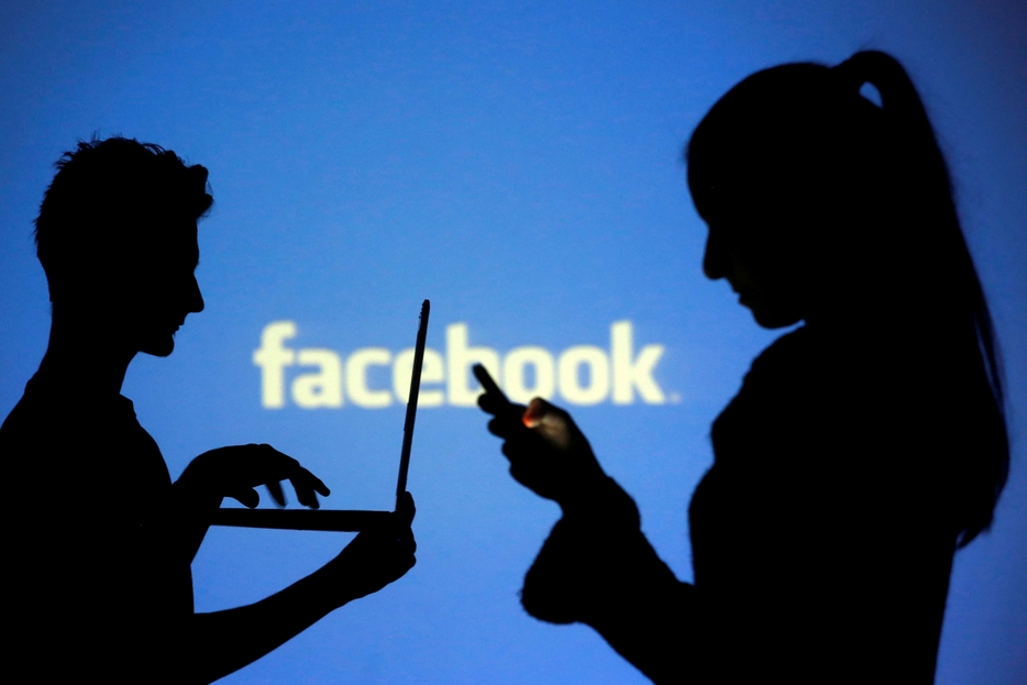 Le ombre di due utenti davanti a un'insegna di Facebook