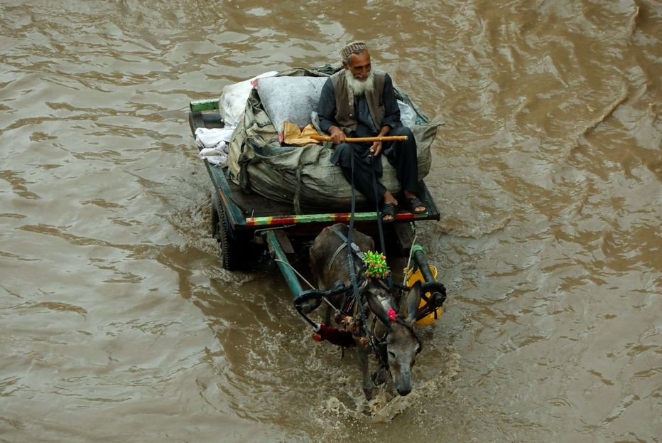 Un uomo guida un carretto trascinato da un asino in una strada allagata dalle piogge monsoniche