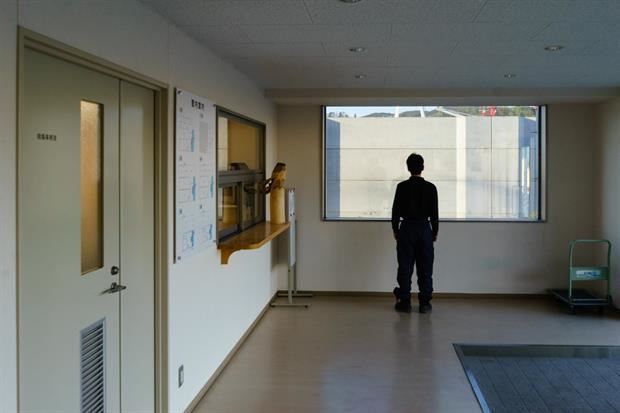 Kesennuma (Miyagi) – 2019.  Un operaio all'interno di una industria per la lavorazione del ghiaccio guarda attraverso la finestra in direzione del mare, con la visuale ostruita da un muro anti-tsunami