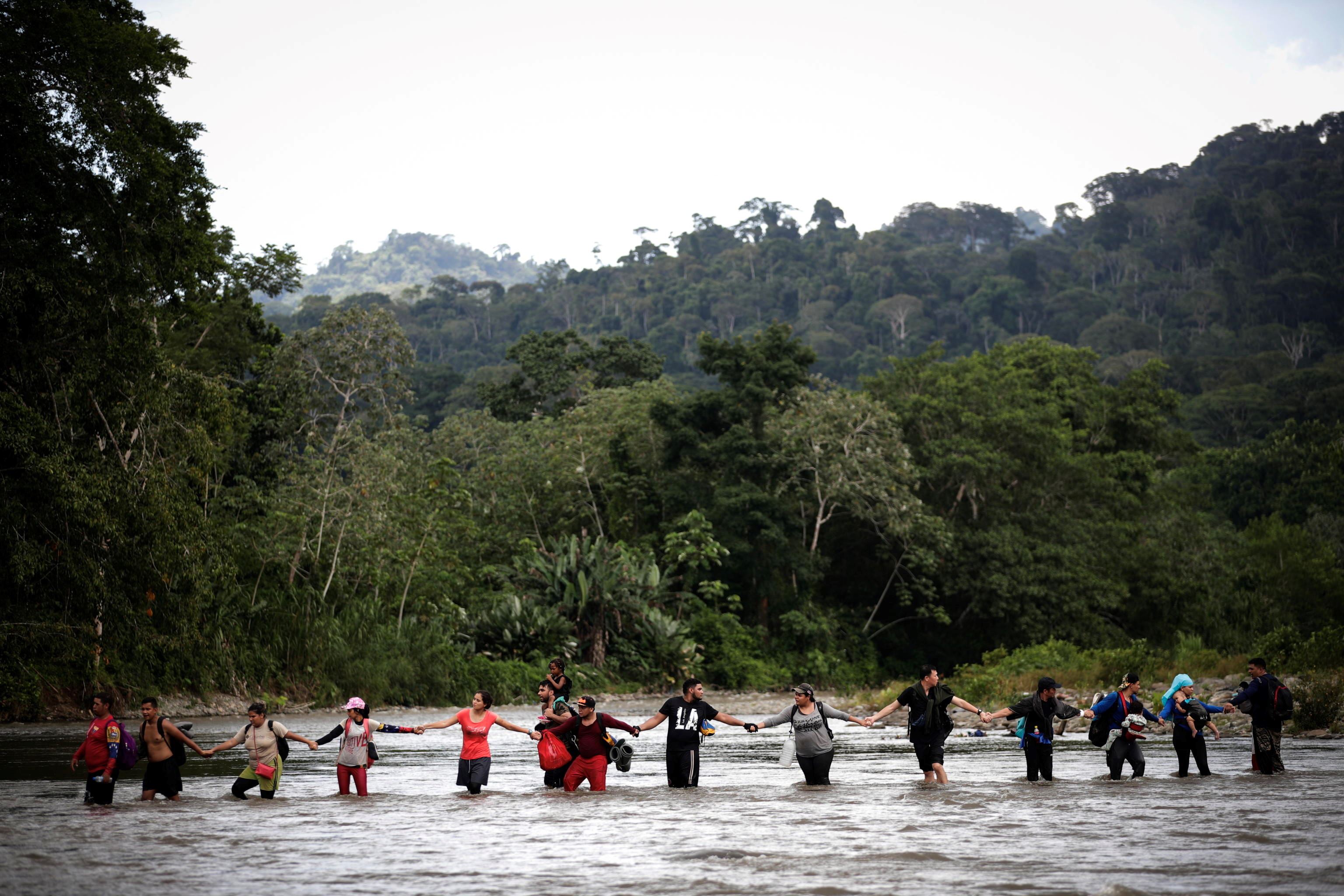 Profughi formano una catena umana per attraversare uno dei molti fiumi della selva del Darién