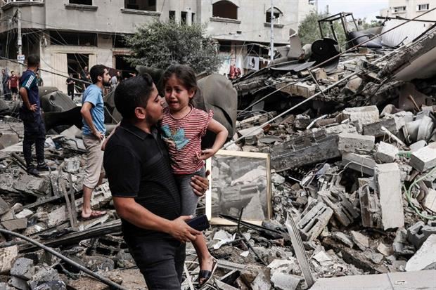 Un uomo tiene in braccio la sua bambina in lacrime davanti a un edificio distrutto durante il contrattacco aereo di Israele nella Striscia di Gaza