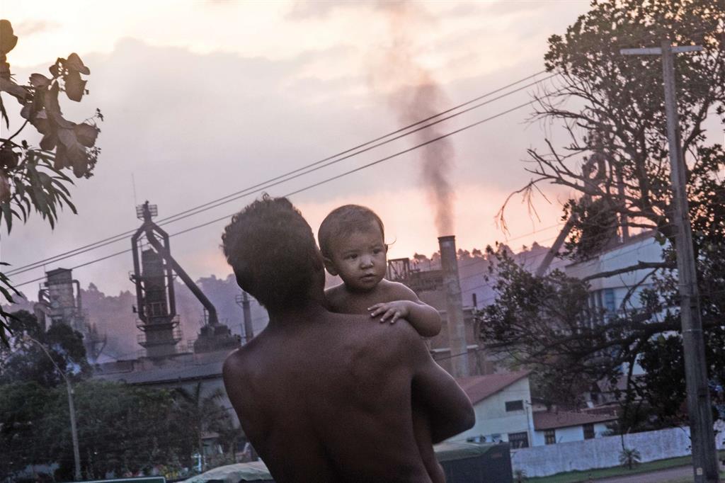 Un papà con il figlio osserva il fumo emesso senza sosta da una fabbrica a ridosso delle case di Piquiá de Baixo (Marcelo Cruz)