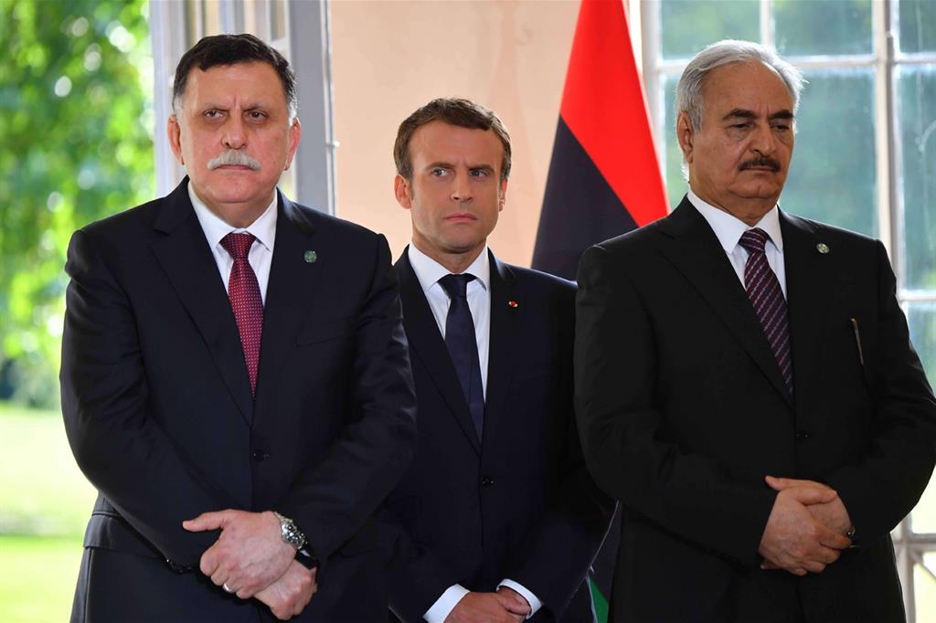 La stretta di mano tra i leader libici al-Sarraj e Haftar. Al centro, Macron