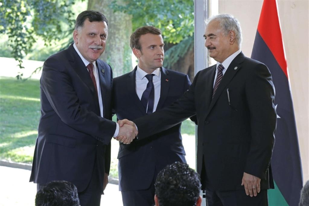 Intesa raggiunta per la Libia a Parigi: al Sarraj (a sinistra) stringe la mano ad Haftar. Tra loro un soddisfatto Macron (Ansa)