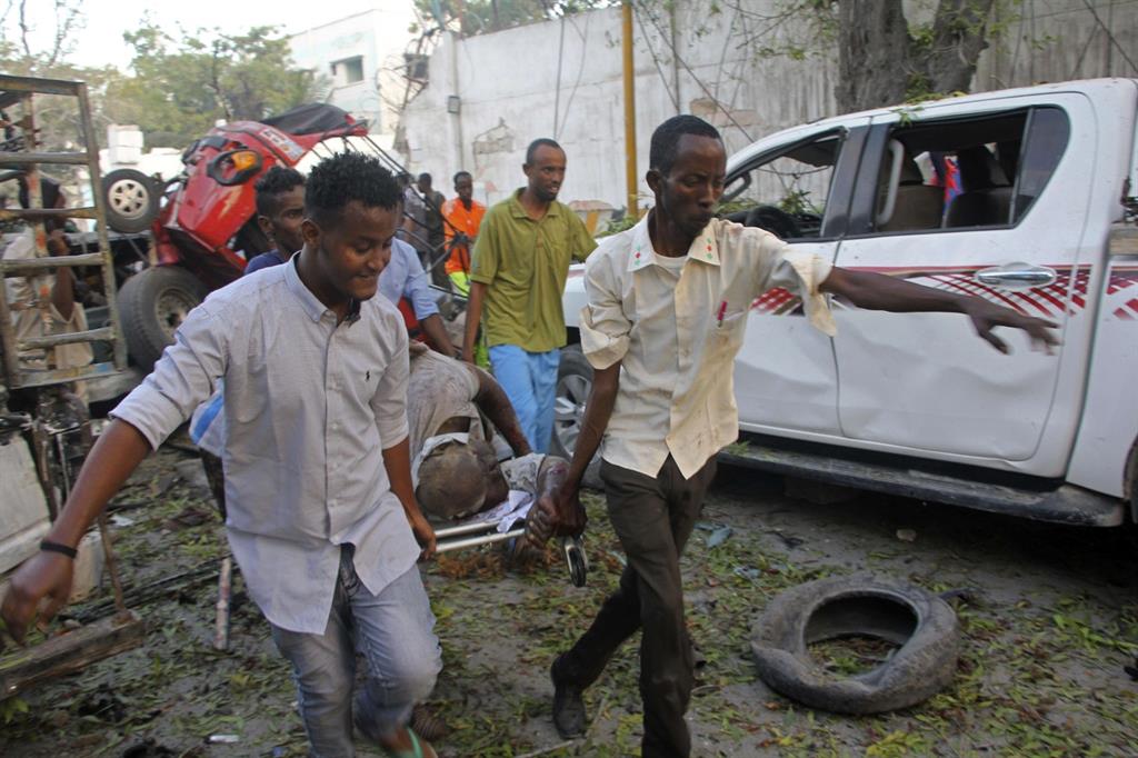 I soccorritori portano via un ferito dopo l'esplosione di un'autobomba in centro Mogadiscio (Ansa)