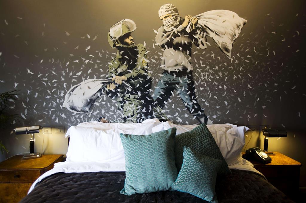 Banksy, un poliziotto israeliano e un palestinese si prendono a cuscinate in una delle sale del The Walled Off Hotel nella città di Betlemme - 