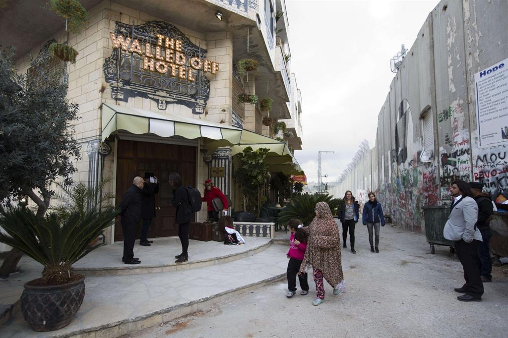 Persone davanti al The Walled Off Hotel a destra si vede il muro di separazione tra la Cisgiordania e Israele