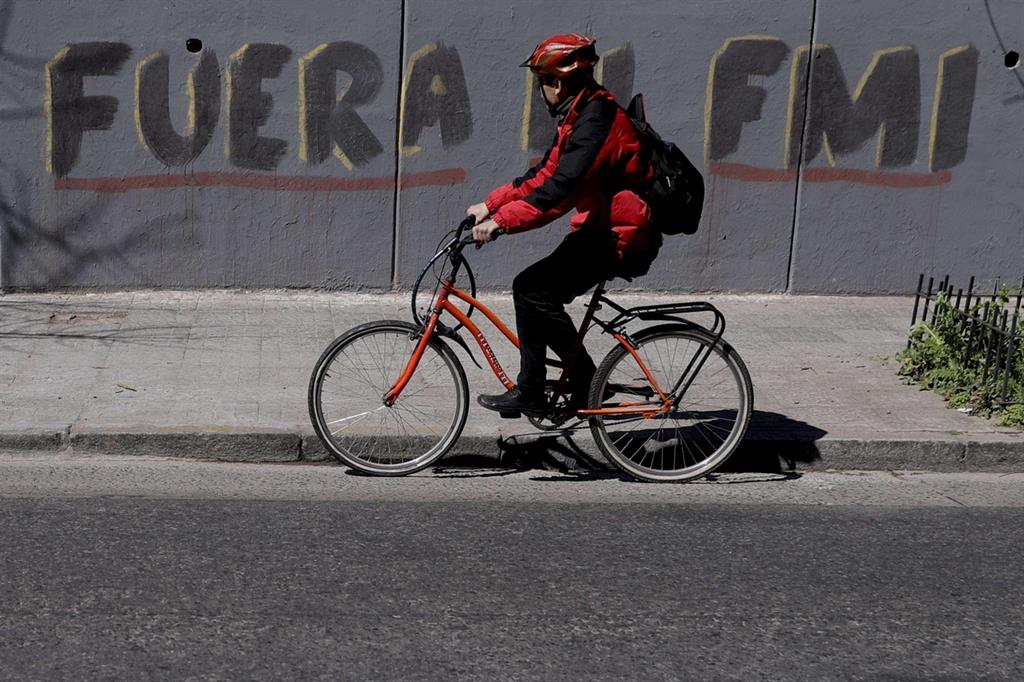 Un ciclista a Buenos Aires: dietro di lui una scritta contro il Fondo Monetario Internazionale (Ansa)