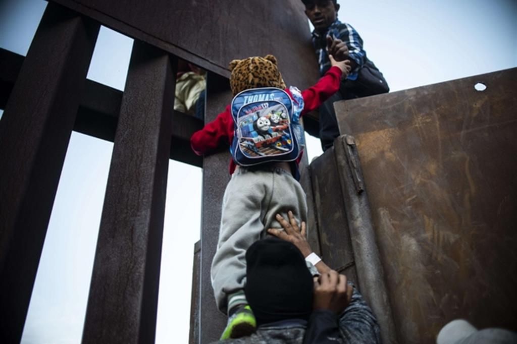 Un ragazzo cerca di scavalcare la barriera di metallo che separa il Messico dagli Stati Uniti