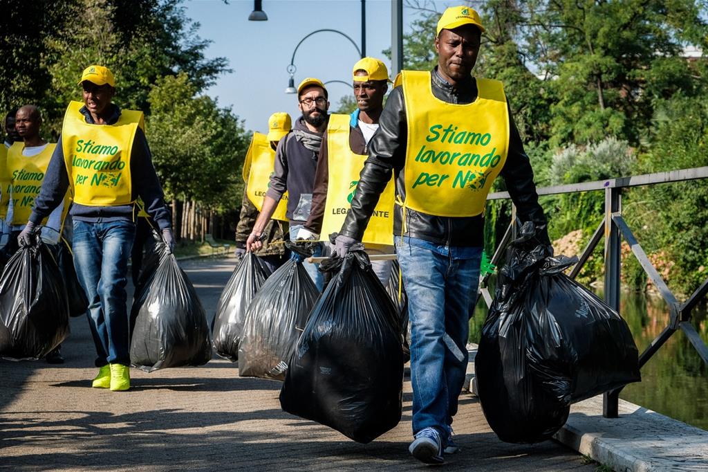 Migranti aiutano a pulire la città durante un'iniziativa di volontariato (Fotogramma)