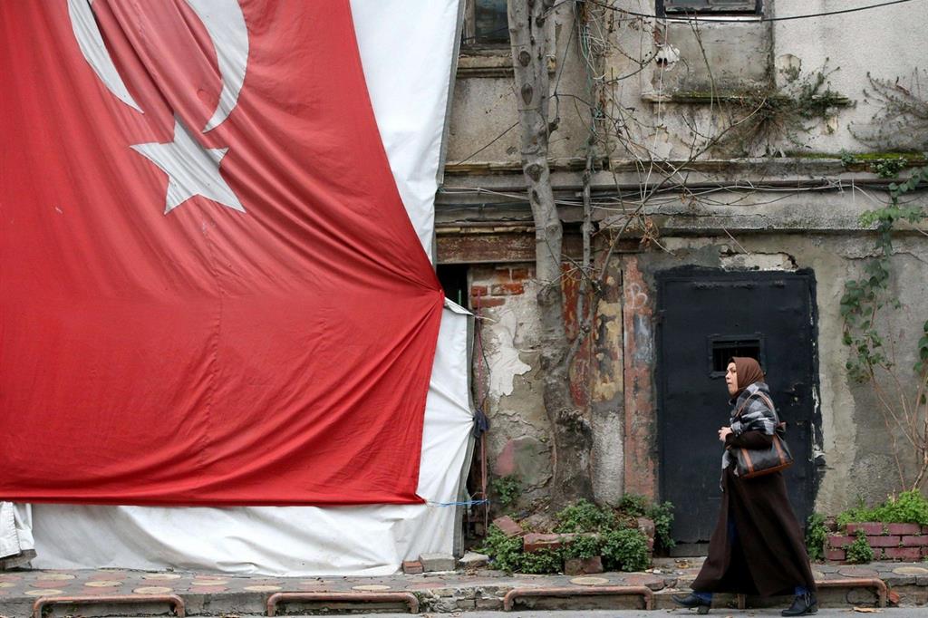 Una donna cammina vicino alla bandiera turca. La violenza sulle donne in Turchia è particolarmente allarmante (Ansa)