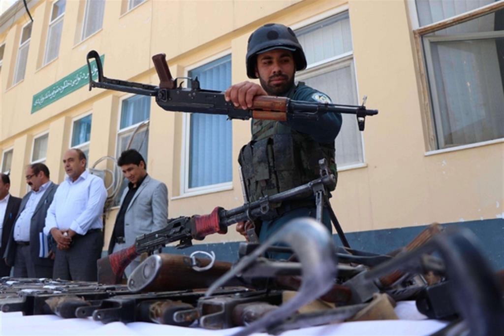 Un poliziotto afghano sorveglia le armi di una milizia illegale che si è arresa (Ansa)