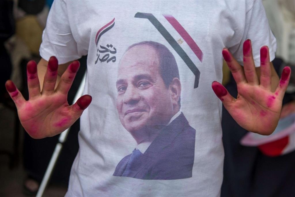 Un sostenitore di al-Sisi, fuori dal seggio con il ritratto del presidente sulla maglietta, mostra i segni dell'inchiostro sulle mani che testimoniano il voto (Ansa)