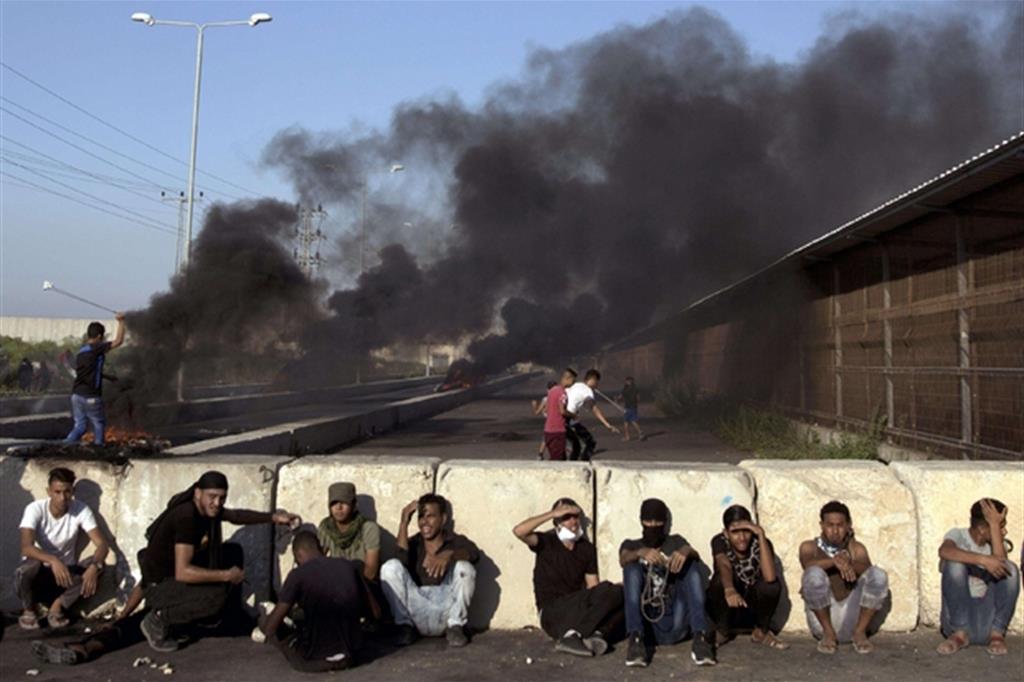 Ragazzi palestinesi si proteggono dai lacrimogeni dietro una barriera a ridosso del valico di Erez (Ansa)