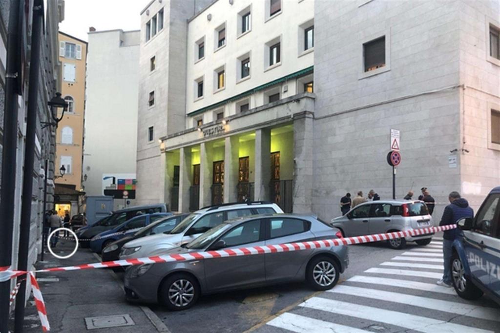 La questura di Trieste dopo la sparatoria. Nel cerchio si vede la pistola usata dall'omicida, caduta sul marciapiedi (Ansa)