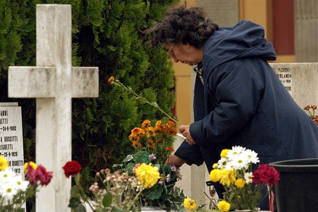 Una donna depone dei fiori su una tomba nel cimitero del Verano a Roma (Ansa)
