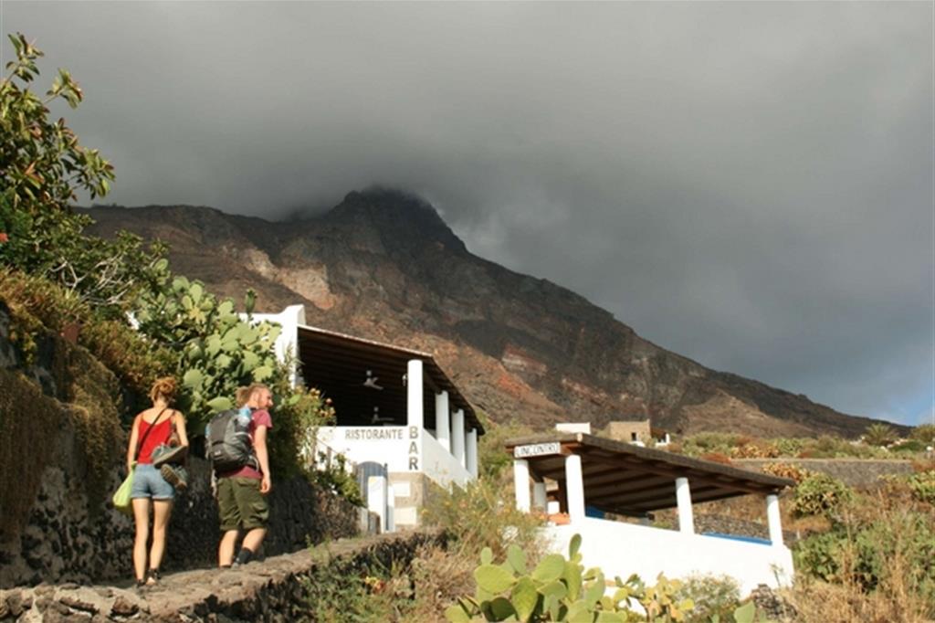 Turisti tra le case di Ginostra. Sullo sfondo lo Stromboli