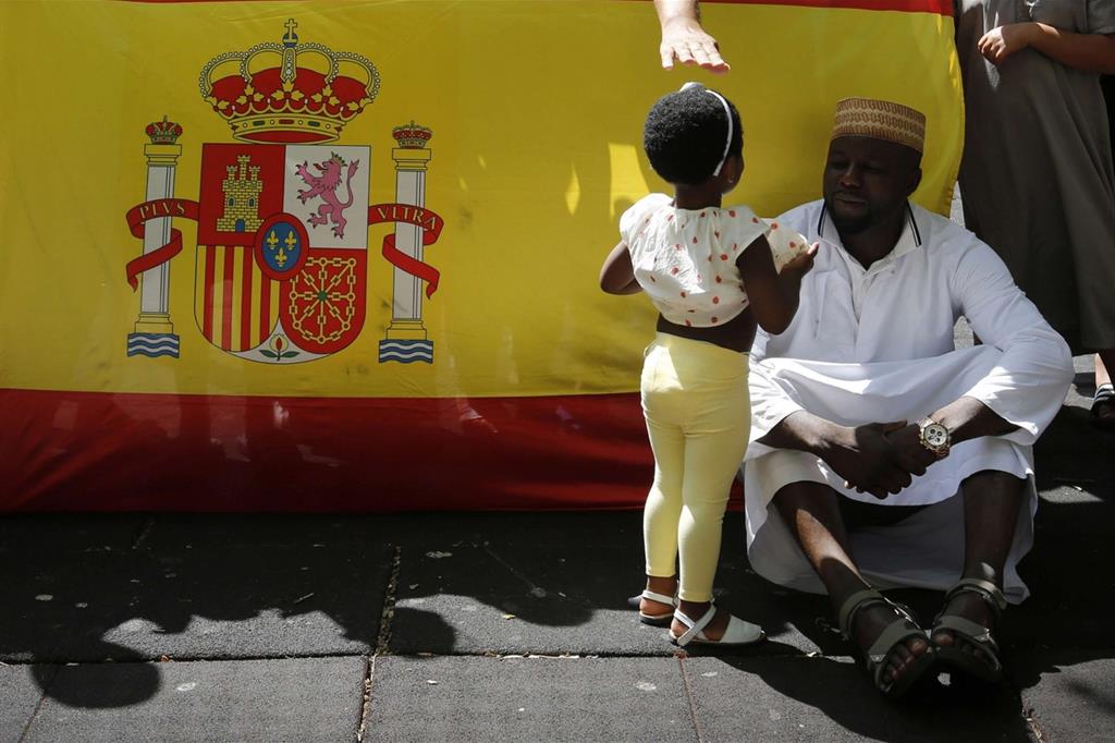 Un padre con la figlia d’origine nordafricana di fronte a una bandiera della Spagna