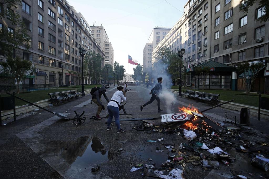 Dimostranti bruciano rifiuti, domenica, nelle strade di Santiago del Cile, dove resta lo stato d'emergenza (Ansa)