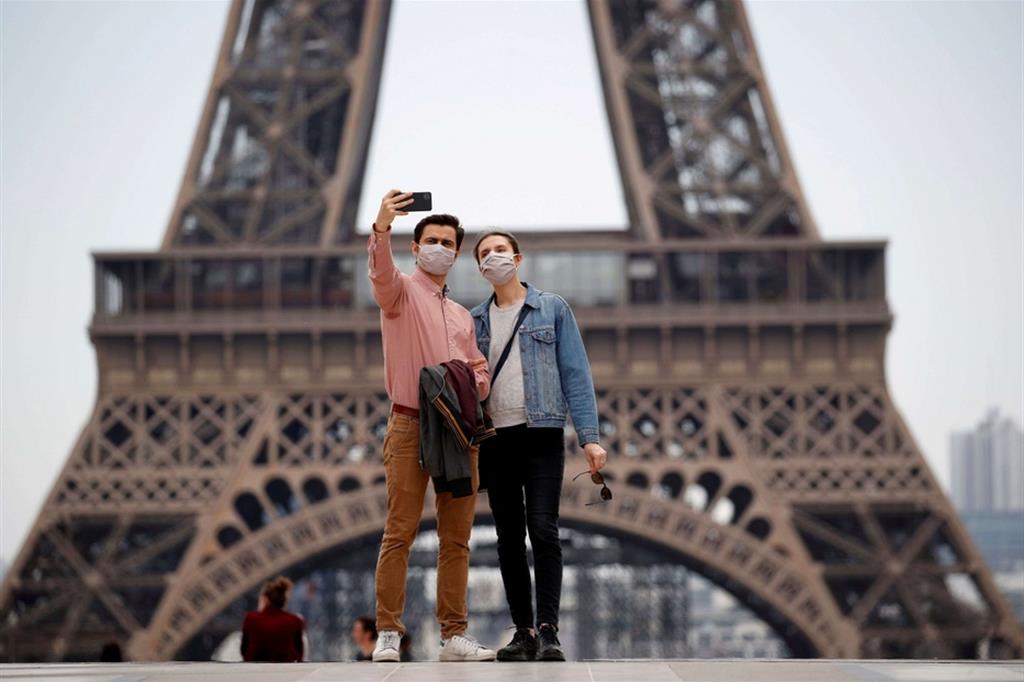 Turisti con la mascherina davanti alla Tour Eiffel. La Francia ha cominciato a uscire dal lockdown l'11 maggio