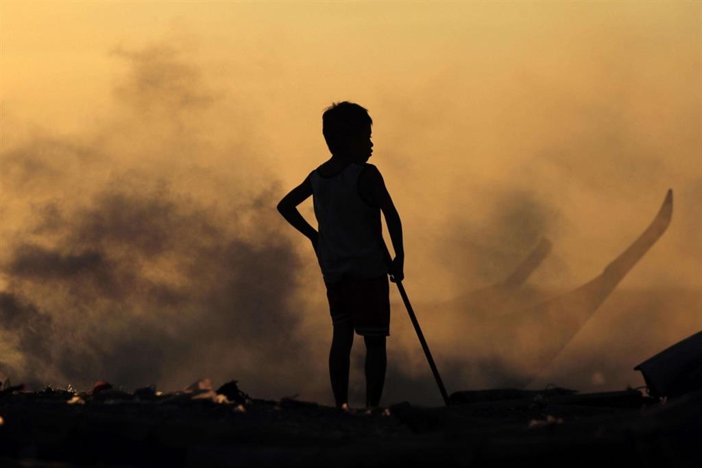 Uno dei tanti “figli delle discariche” tra il fumo dei rifiuti bruciati a Manila, nelle Filippine