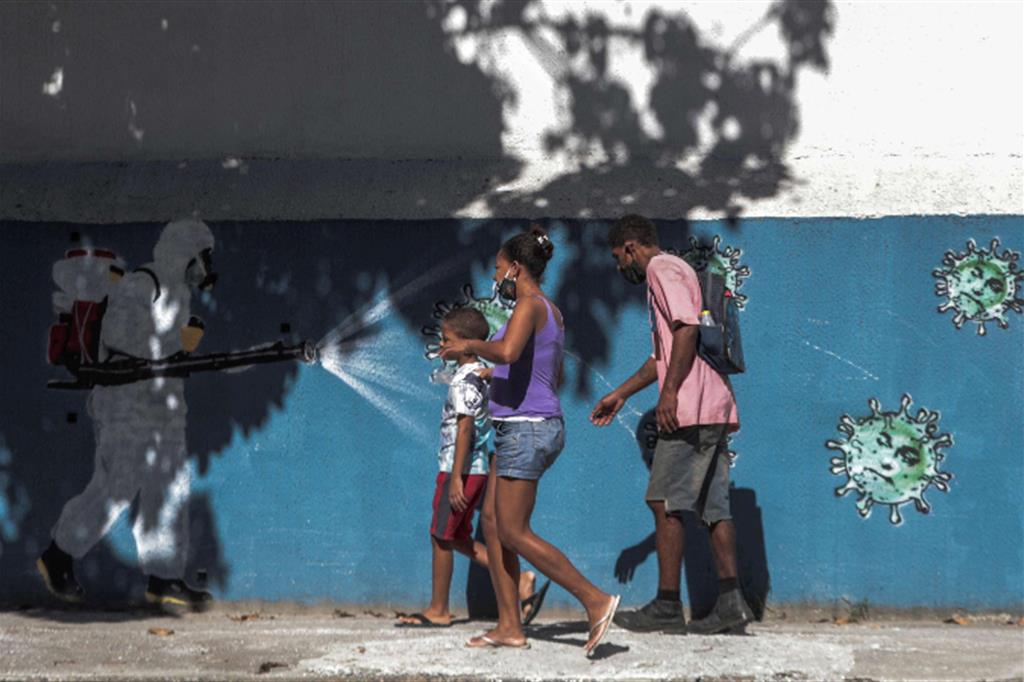 Una famiglia a Rio de Janeiro davanti a un murales in cui un operaio spruzza disinfettante su del coronavirus con il volto di Biolsonarocon 