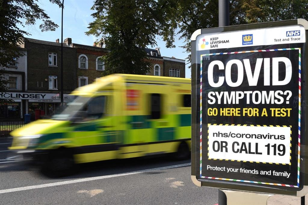 Un'ambulanza, a Londra, passa vicino a un cartello che invita a fare il test per Covid-19 in caso di sintomi sospetti
