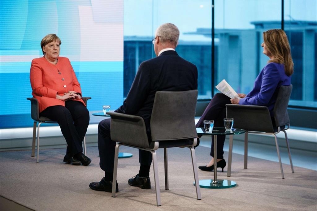 a cancelliera Angela Merkel dialoga con due giornalisti durante un’intervista al canale tv Ard