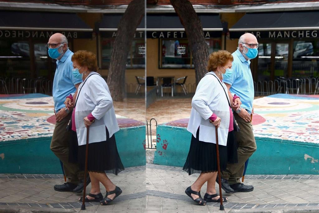 Una coppia di anziani si riflette in un vetro mentre passeggiano nel quartiere di Usera, a Madrid
