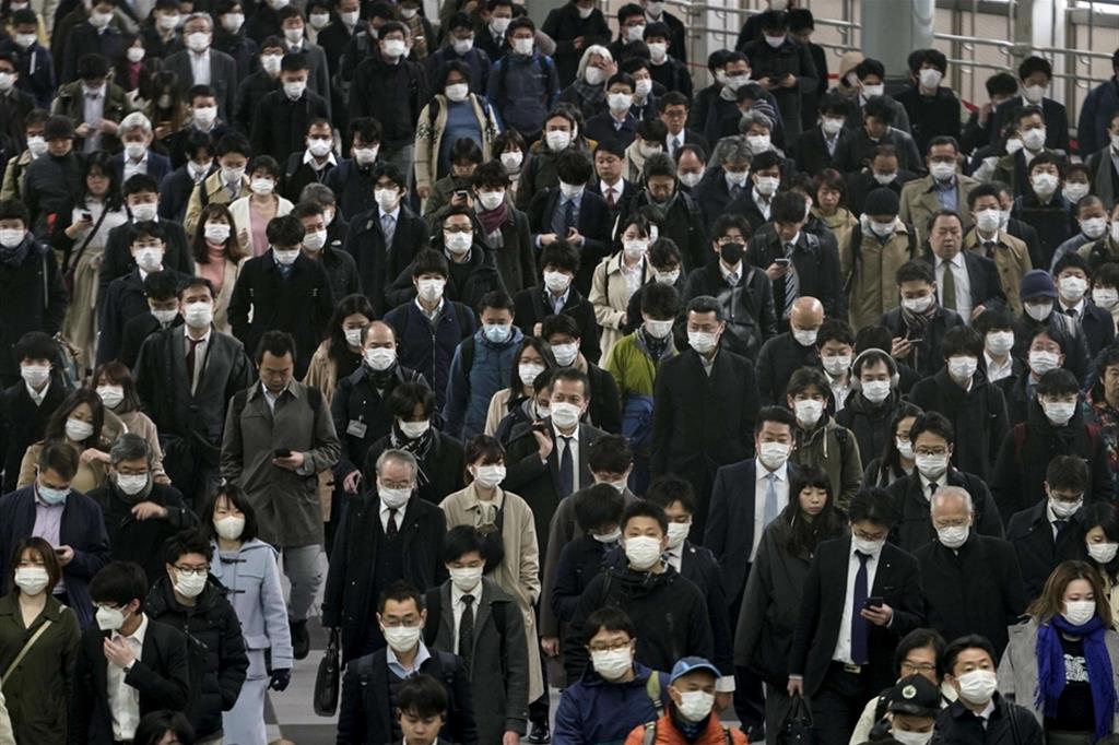 Un esercito di impiegati, protetti da una semplice mascherina, si avvia in massa al un ingresso della metropolitana di Tokyo