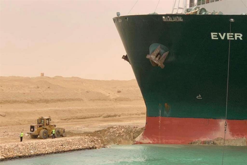 Il gigante e il piccoletto: ai piedi del mega portacontainer una ruspa cerca di rimuovere la sabbia in cui è andato a incagliarsi