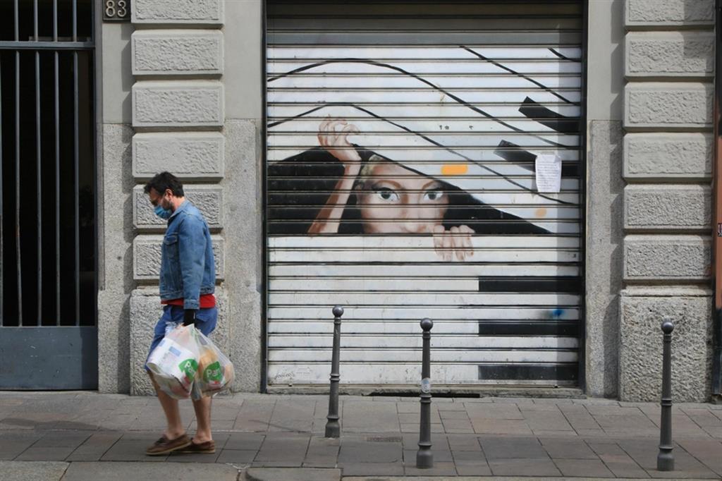 Cittadini milanesi camminano davanti a serrande di negozi chiusi durante i primi mesi della pandemia