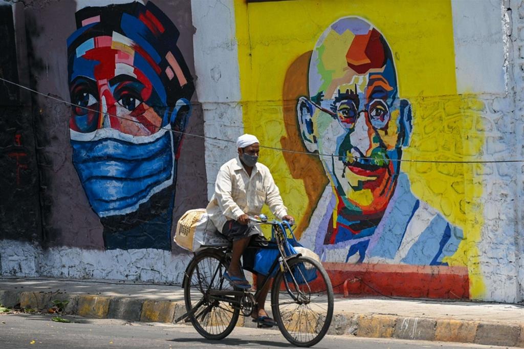 In india la pandemia sta esplodendo. Nell'ultima settimana si sono registrati 1,6 milioni di nuovi contagi. Nella foto: Mumbai, un uomo pedala davanti a un murales del Mahatma Gandhi