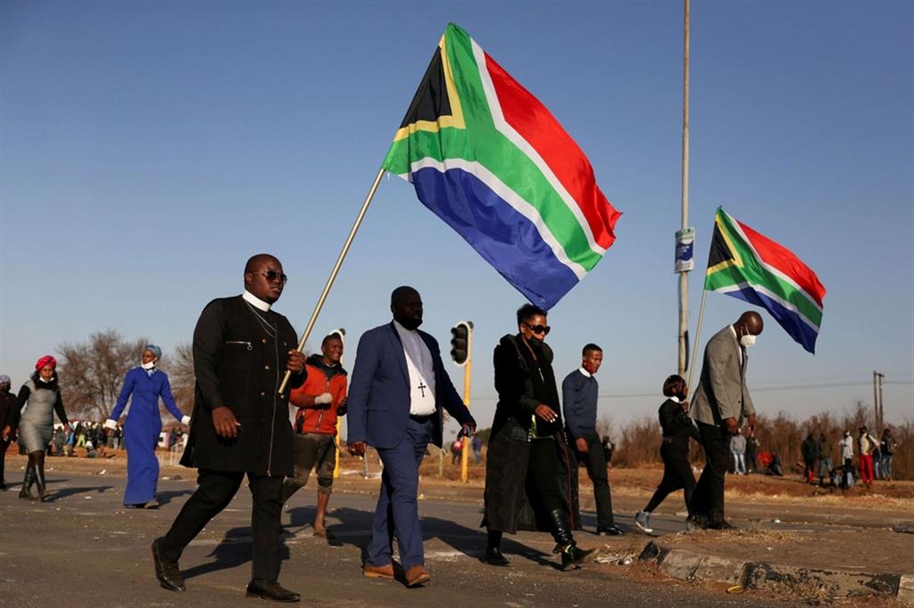 Leader religiosi sfilano con la bandiera sudafricana vicino a un centro commerciale saccheggiato dai rivoltosi