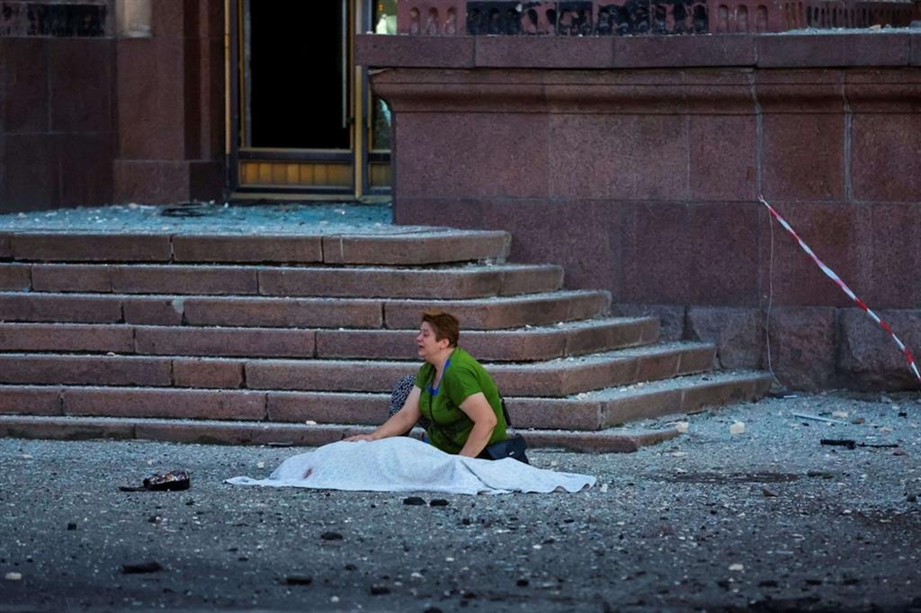 Una donna inginocchiata davanti al corpo della mamma dopo un bombardamento in una cittadina dell'oblast di Donetsk