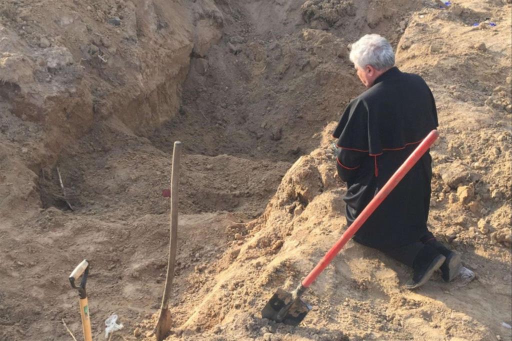 Il cardinale Konrad Krajewski prega davanti a una fossa comune
