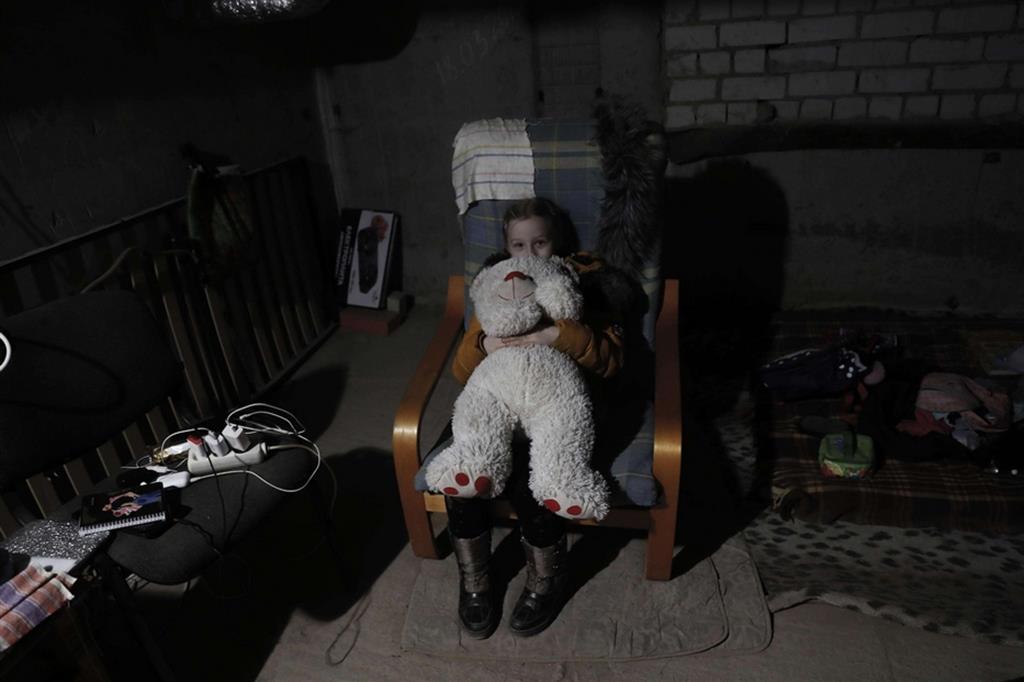 Yarina, 7 anni, abbracciata al suo grande pupazzo. Non sappiamo se indossi gli stivali anche quando va a dormire, nel freddo dello scantinato - Ansa